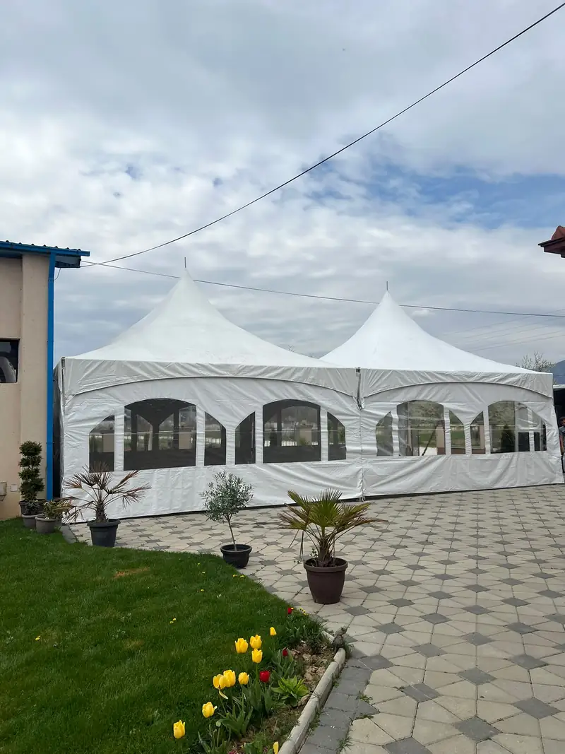 Две бели тенди со странични платна и прозорци на поплочен двор